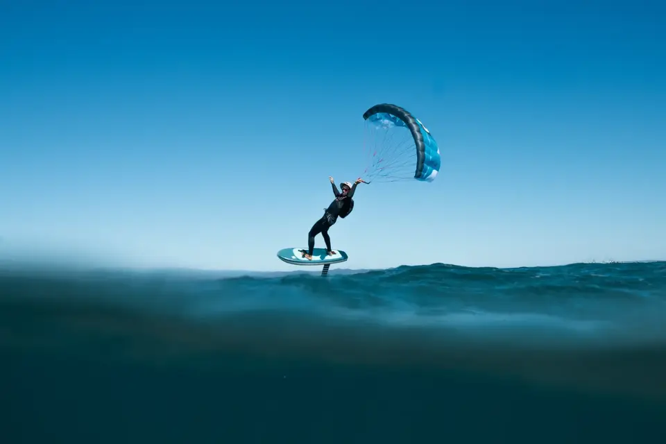 Un rider en parawing sous une aile bleue, sur une mer bleu profond sous un ciel dégagé