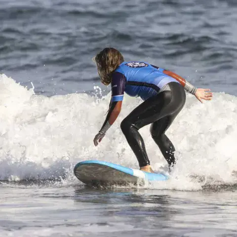 Élève de surf debout sur une planche dans l'écume