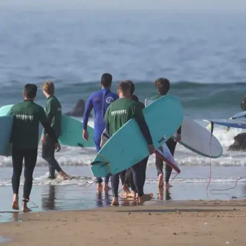Élèves en combinaison se dirigeant vers l'eau avec leurs planches