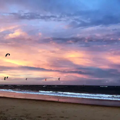 Plage au coucher du soleil avec kites au loin