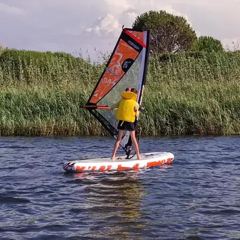 Windsurfeur sur un plan d'eau calme bordé de roseaux