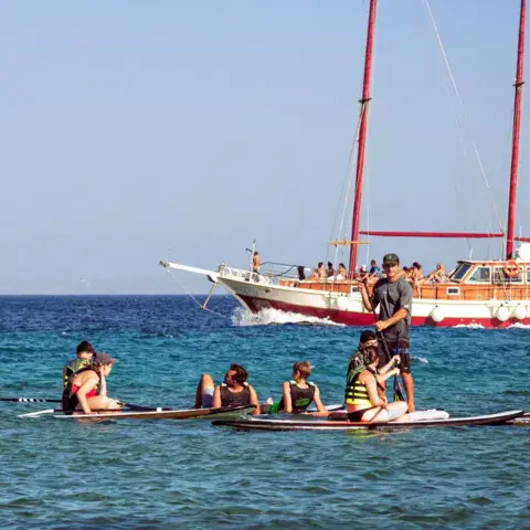 Groupe de stand up paddle devant un voilier