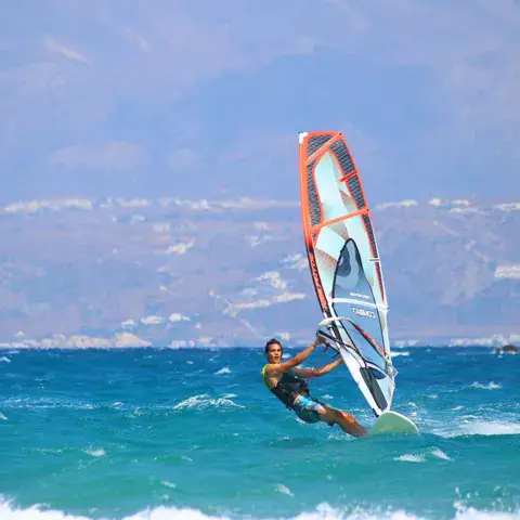 Windsurfeur sur une eau turquoise, côte au fond