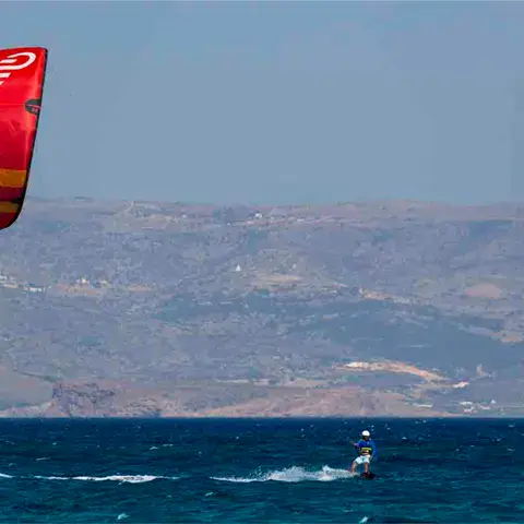 Kitesurfeur sous une aile rouge, côte au fond