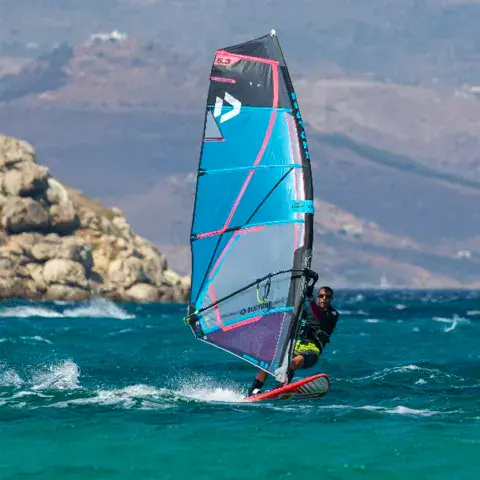 Windsurfeur sous une voile bleue devant des rochers