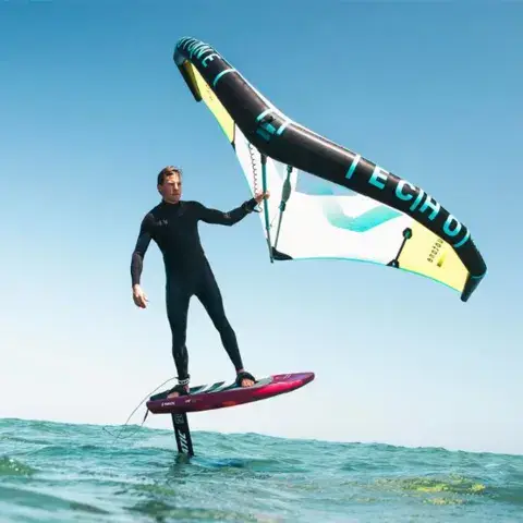 Rider de wingfoil debout sur sa planche, aile en main