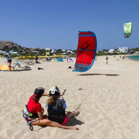 Plage de sable avec ailes de kite gonflées et élèves assis