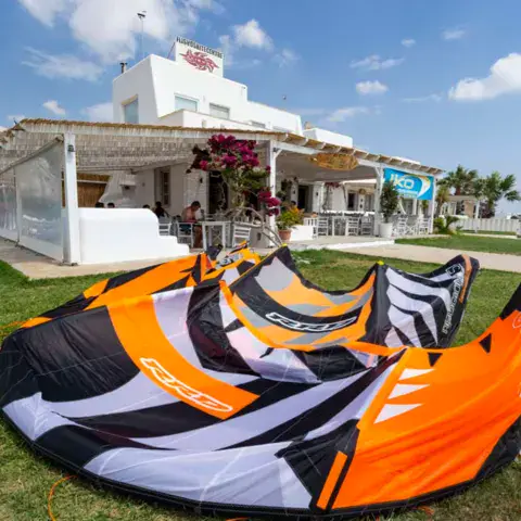 Aile de kite orange posée sur l'herbe devant un bâtiment blanc