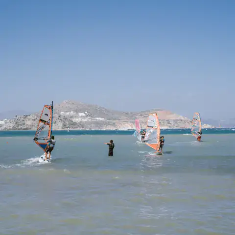Plusieurs windsurfeurs sur une eau calme, côte au loin