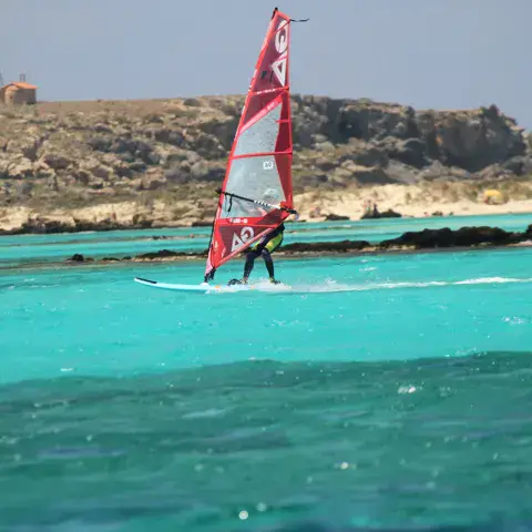Windsurfeur sous voile rouge devant la côte