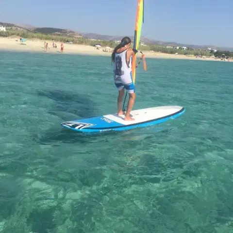 Windsurfeur debout sur sa planche dans une eau turquoise