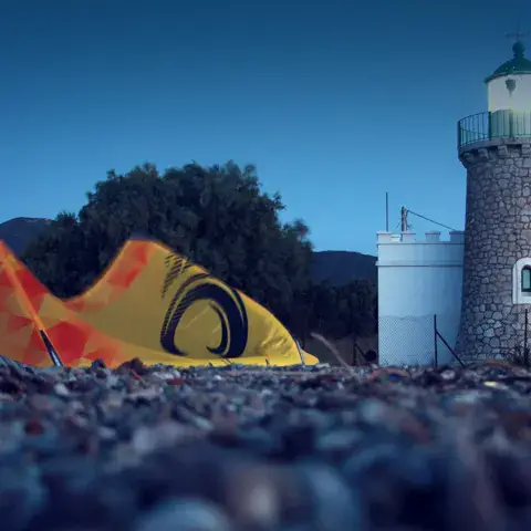 Aile de kitesurf posée sur les galets devant un phare