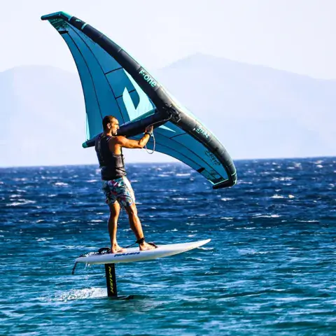Rider de wingfoil debout sur sa planche, aile bleue en main