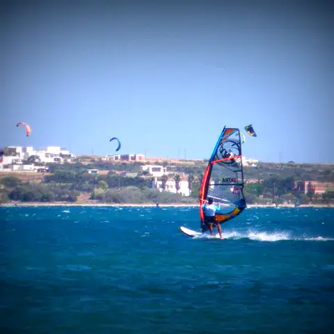Windsurfeur sous une voile rouge et bleue, côte en arrière-plan