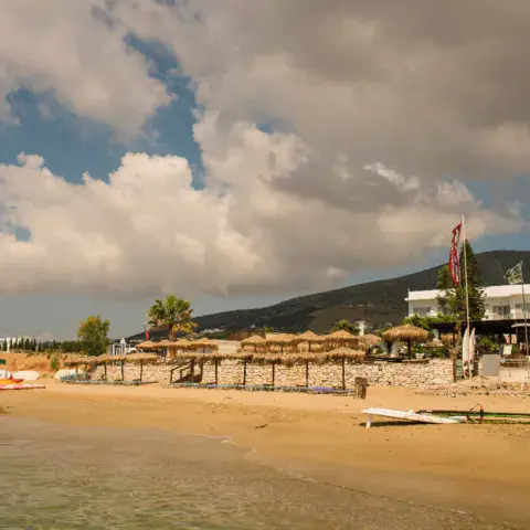 Plage de sable avec parasols en paille et bâtiment en fond
