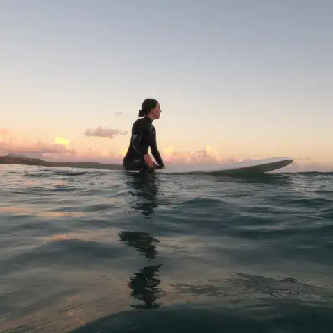 Surfeuse assise sur sa planche au coucher du soleil