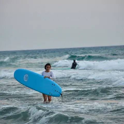 Surfeuse avec sa planche bleue dans les vagues