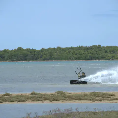 Kitesurfeur glissant en soulevant des gerbes d'eau, aile rouge dans le ciel