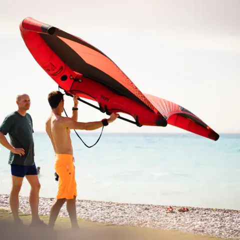 Deux riders portant une aile de wing foil sur la plage