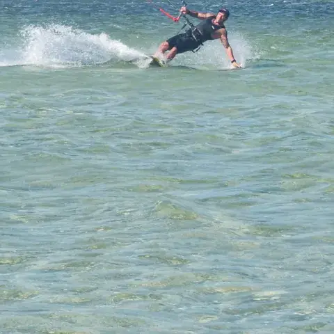 Kites étalés sur la plage avec des kitesurfeurs au loin