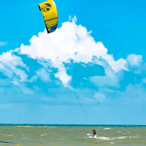 Kitesurfeur sous un kite jaune devant un ciel nuageux