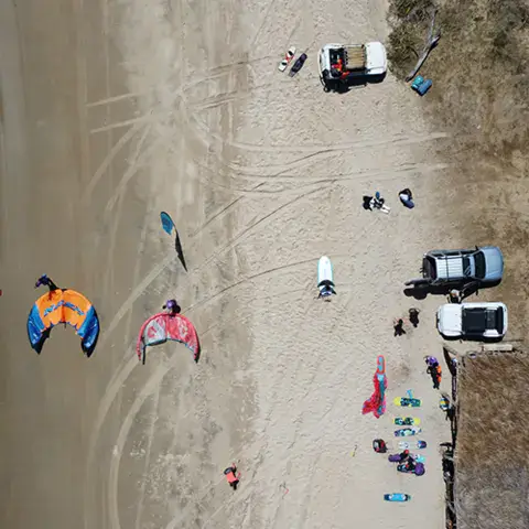 Vue aérienne d'une plage avec kitesurfeurs et véhicules