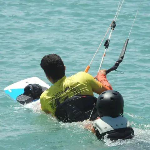 Élève dans l'eau avec sa barre de kite et sa planche