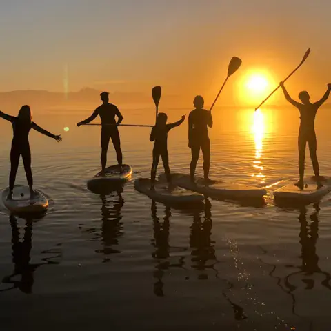 Groupe de pagayeurs debout sur l'eau au coucher du soleil