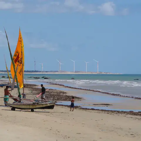 Plage avec des bateaux à voile sur le sable et des éoliennes au loin