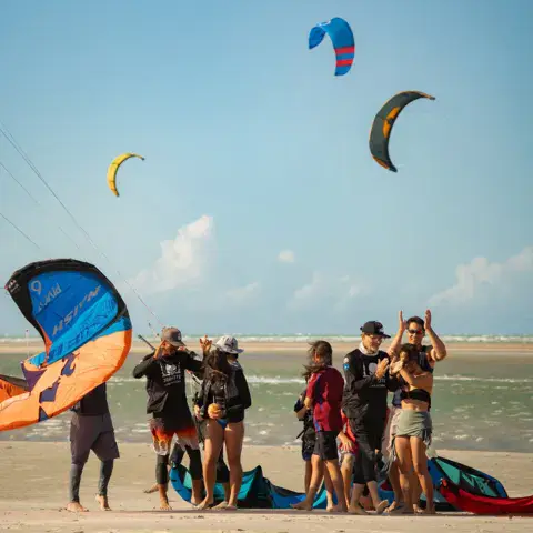Plage avec de nombreux kites en l'air et des kitesurfeurs au sol