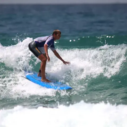 Élève debout sur une vague pendant un cours de surf