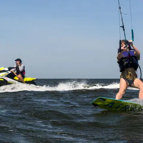 Élève de kitesurf sur sa planche, jet-ski de support derrière
