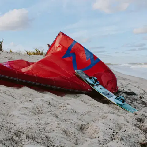 Aile de kite rouge posée sur le sable avec une planche