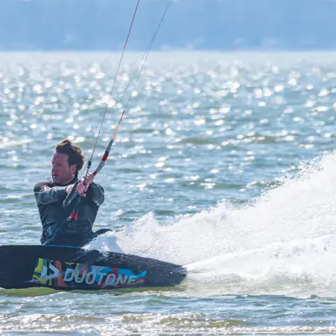 Kitesurfeur sur sa planche, gerbe d'eau derrière lui