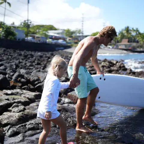 Moniteur et enfant entrant dans l'eau sur les roches de la baie