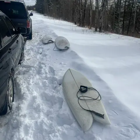 Planches de surf posées dans la neige au bord d'une route, en hiver