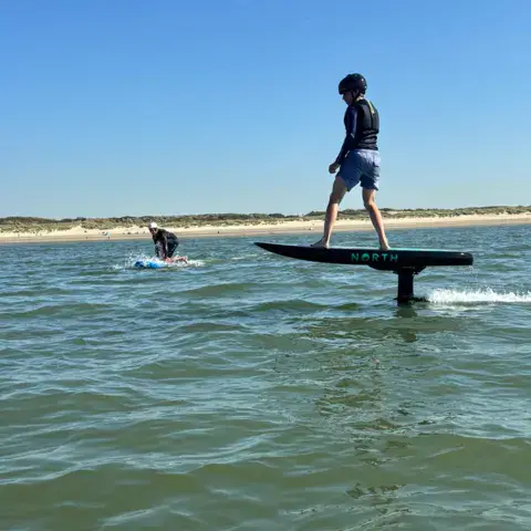 Pratiquant debout sur une planche à foil, sur l'eau plate