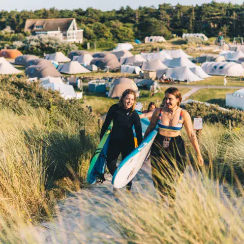 Camp de tentes dans les dunes, avec deux surfeuses et leurs planches