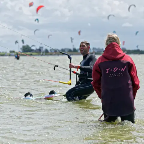 Moniteur et élève dans l'eau, avec des kites au fond