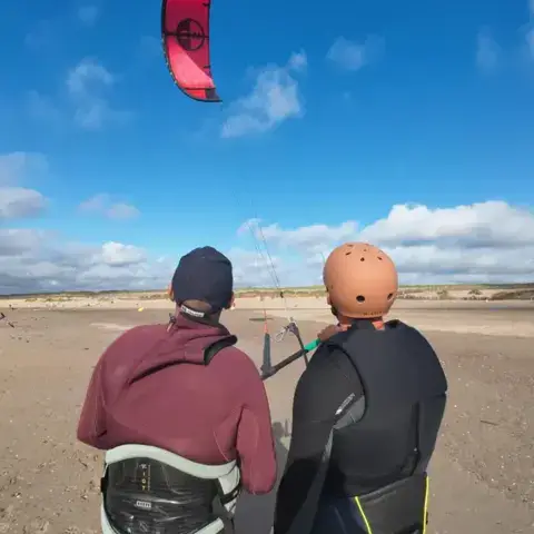 Deux kitesurfeurs sur une plage de sable, kite en vol
