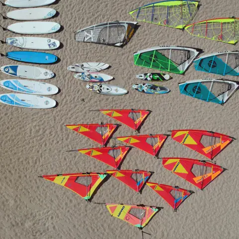 Planches et voiles de windsurf alignées sur le sable, vues du ciel