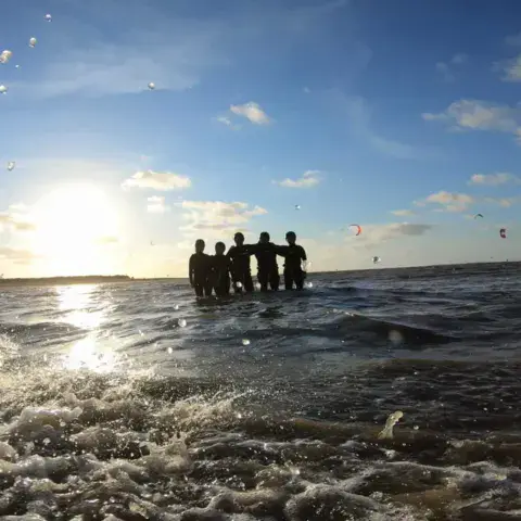 Groupe d'élèves dans l'eau, kites au coucher du soleil