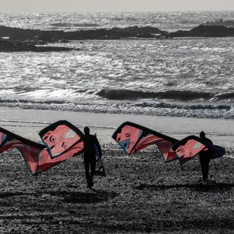Deux kitesurfeurs portant leurs ailes sur la plage