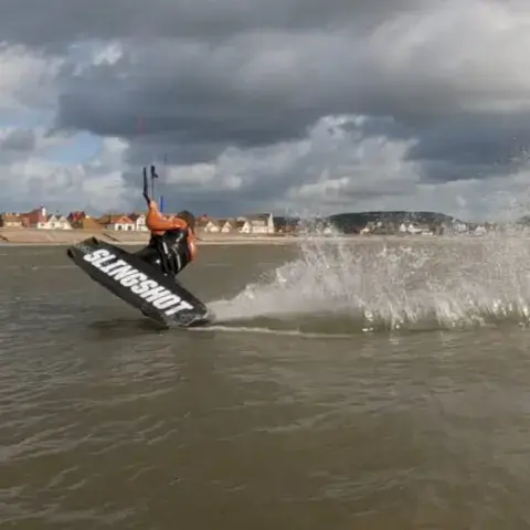 Kitesurfeur dérapant sur l'eau plate avec gerbe d'écume