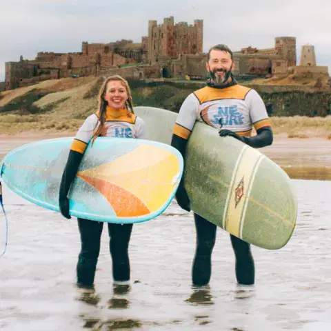 Deux moniteurs avec leurs planches devant le château de Bamburgh