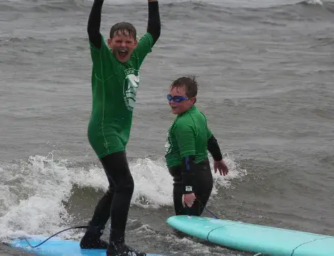 Deux jeunes élèves bras levés dans l'eau, planches à côté