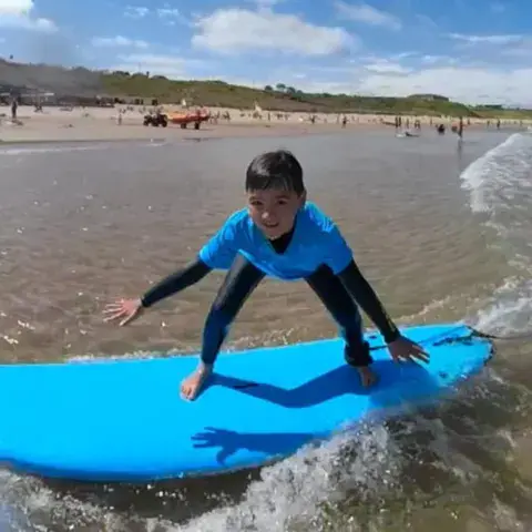 Jeune élève debout sur une planche bleue dans les vaguelettes