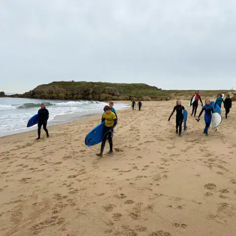 Groupe marchant vers l'eau avec ses planches sur la plage