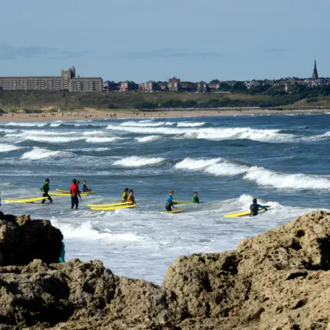 Séance de surf dans les vagues, devant les rochers et la côte