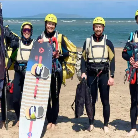 Groupe d'élèves équipés de casques et de gilets, avec une planche de kite